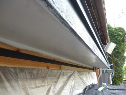 Close-up of a house soffit under renovation: white-painted underside, wooden beam support, and plastic sheeting along the wall.