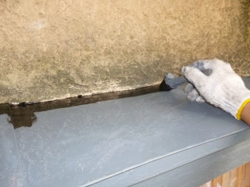 Gloved hand applying gray sealant along a metal roof seam.