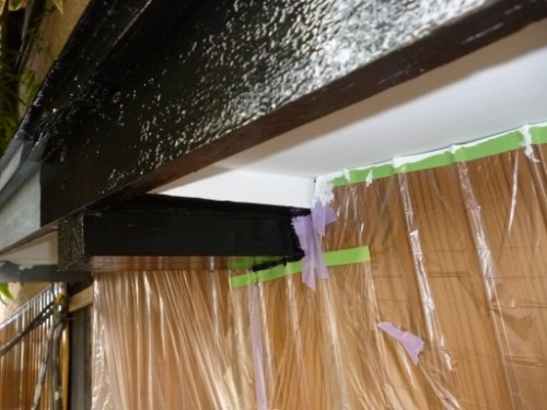 Construction area showing a black painted ceiling beam and protective plastic sheeting taped to the walls for renovation work.