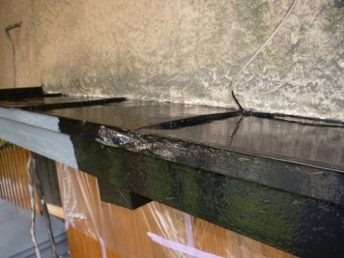 Close-up of a damp, mossy black window sill or edge along a rough concrete wall with a loose wire nearby.