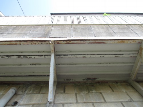 Rusty metal overhang above a concrete wall, with peeling paint and rust stains; a white pipe visible in the lower left.