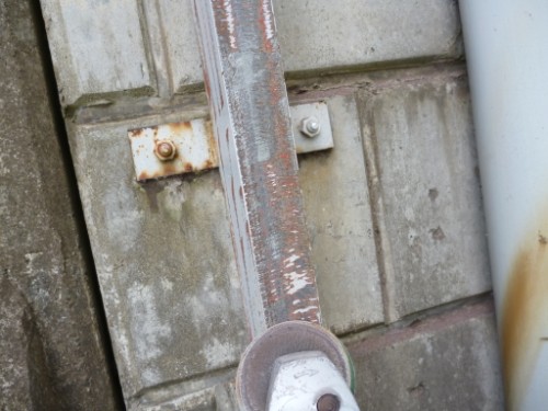 Close-up of a rusted metal lever/latch attached to a weathered concrete wall.