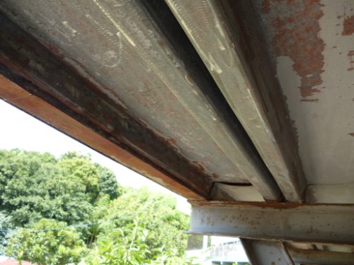 Close-up of a rusted metal beam under a structure with green trees in the background.