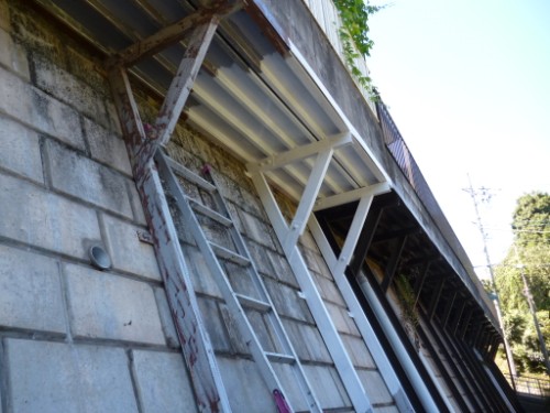 Scaffolding and a leaning ladder against a concrete block wall beneath an elevated metal structure, suggesting ongoing construction or maintenance outdoors.