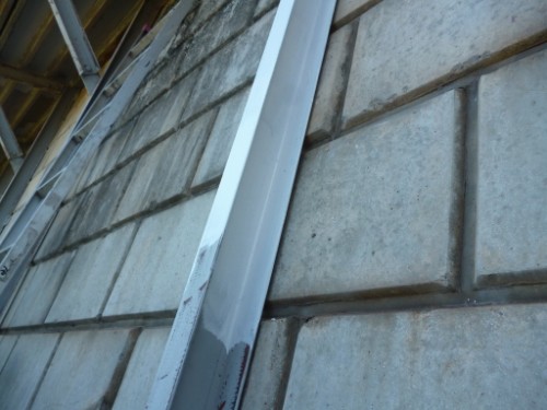 Aluminum metal flashing strip running vertically along a concrete block wall in a construction site.