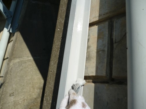 Person wearing a glove wiping a white metal frame with a cloth outdoors near a doorway or window.