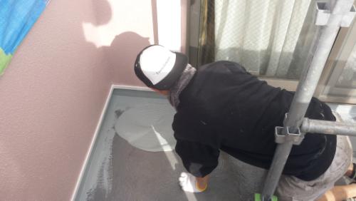 koushin_20140121hiraba | 外壁塗装は神奈川県横浜市の塗装職人 Construction worker wearing a hard hat kneels on a balcony, troweling fresh concrete along the edge near a pink wall with scaffolding nearby