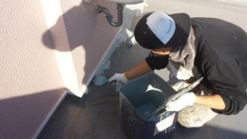 koushin_20140121tatiagari2 | 外壁塗装は神奈川県横浜市の塗装職人 Person wearing a helmet and gloves paints an outdoor pink wall with a brush, a blue paint bucket beside them.