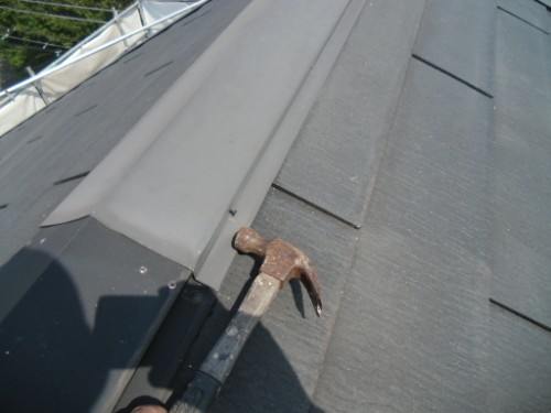 koushin_CIMG2581-1 | 外壁塗装は神奈川県横浜市の塗装職人 Hammer resting on a sloped roof beside metal flashing and overlapping shingles during roofing work