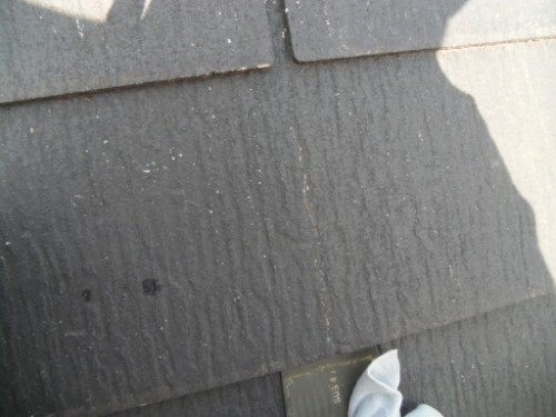 koushin_CIMG2583-1 | 外壁塗装は神奈川県横浜市の塗装職人 Shaded close-up of dark gray asphalt shingles on a roof, with a shadow of a person and part of a white sneaker visible along the bottom edge.