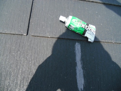 Green tube of adhesive lying on dark pavement next to a white chalk line, with a large shadow of a person in the foreground