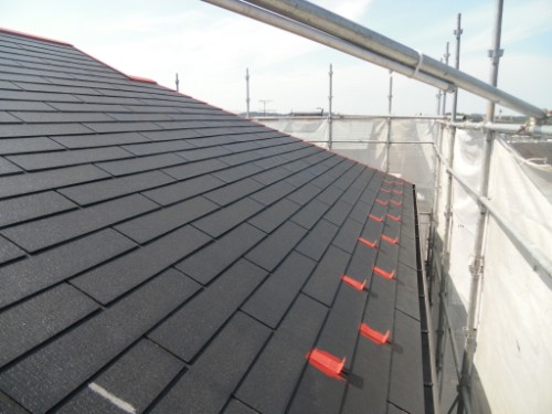koushin_CIMG2594-1 | 外壁塗装は神奈川県横浜市の塗装職人 Sloped roof with dark asphalt shingles under construction; red clips line the edge while scaffolding surrounds the area.