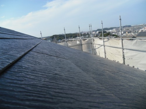 koushin_CIMG2597-1 | 外壁塗装は神奈川県横浜市の塗装職人 Close-up of a dark slate roof with scaffolding and a distant town under a blue sky.