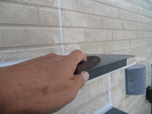 koushin_CIMG2605-1 | 外壁塗装は神奈川県横浜市の塗装職人 Person's hand scrubs a metal trim along a brick wall with a brown abrasive pad.