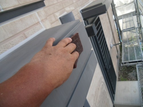 koushin_CIMG2606-1 | 外壁塗装は神奈川県横浜市の塗装職人 Hand scrubbing a gray metal railing with a brown abrasive pad on an exterior building, scaffolding visible in the background.