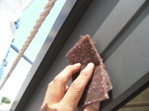 koushin_CIMG2614-1 | 外壁塗装は神奈川県横浜市の塗装職人 Hand cleaning a window frame with a brown abrasive sponge outdoors.