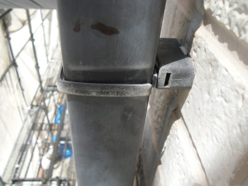 koushin_CIMG2617-1 | 外壁塗装は神奈川県横浜市の塗装職人 Close-up of a gray metal pipe clamped to a brick wall with a plastic bracket on a construction site