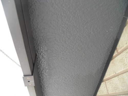 koushin_CIMG2622-1 | 外壁塗装は神奈川県横浜市の塗装職人 Close-up of a textured gray metal door frame edge with a small hinge plate on the left and brick wall to the right.
