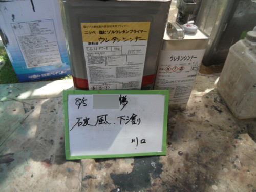 koushin_CIMG2623-1 | 外壁塗装は神奈川県横浜市の塗装職人 Metal containers and bottles labeled in Japanese sit on a stained workbench; a whiteboard in front has handwritten Japanese notes.