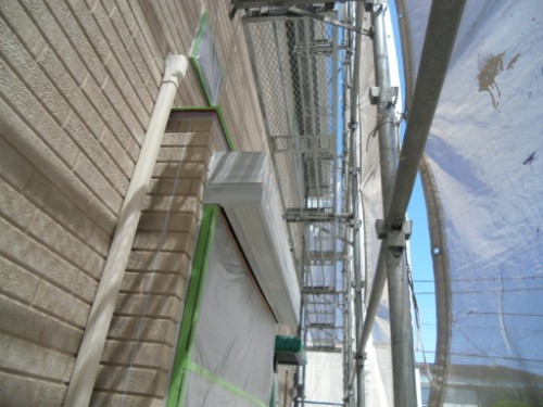 koushin_CIMG2625 | 外壁塗装は神奈川県横浜市の塗装職人 Scaffolding along a brick wall with protective plastic sheets, tape, and metal planks against a blue sky.