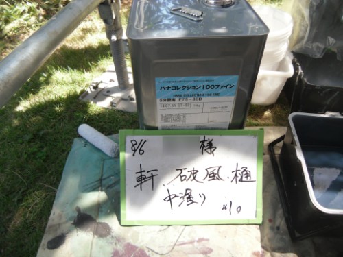 koushin_CIMG2630 | 外壁塗装は神奈川県横浜市の塗装職人 Metal storage container with a label on top, placed near a white signboard with handwritten Japanese notes, outdoors on grass and equipment nearby.