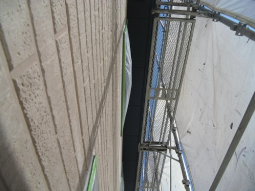 koushin_CIMG2632 | 外壁塗装は神奈川県横浜市の塗装職人 Scaffolding along a brick building wall, with a narrow gap and protective plastic sheeting visible on the right side.