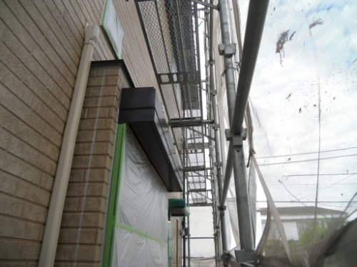 koushin_CIMG2639 | 外壁塗装は神奈川県横浜市の塗装職人 Scaffolding along a brick wall with plastic sheeting and green tape sealing a doorway, indicating ongoing construction work.