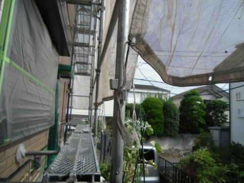 koushin_CIMG2642 | 外壁塗装は神奈川県横浜市の塗装職人 Construction scaffolding along a house with protective tarp and nets, viewed from a narrow platform path.
