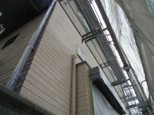 koushin_CIMG2648 | 外壁塗装は神奈川県横浜市の塗装職人 Scaffolding and construction netting along a beige brick building, viewed from below.