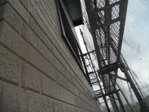 koushin_CIMG2651 | 外壁塗装は神奈川県横浜市の塗装職人 Side view of a beige brick wall with a metal fire escape ladder and grated platform, viewed at an angle.