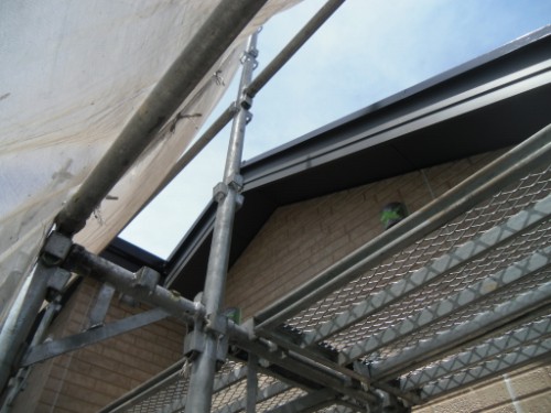 koushin_CIMG2656 | 外壁塗装は神奈川県横浜市の塗装職人 Scaffolding frames against a brick building with a small green bird perched near the roofline.