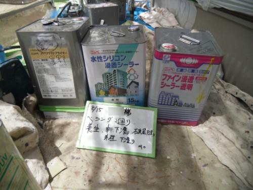 koushin_CIMG2657 | 外壁塗装は神奈川県横浜市の塗装職人 Three metal cans of silicone sealant with Japanese labels sit on a weathered tarp-covered surface, a whiteboard with handwritten notes placed in front.