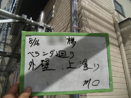 koushin_CIMG2661 | 外壁塗装は神奈川県横浜市の塗装職人 Hand holding a small whiteboard with handwritten notes about balcony exterior wall coating work; date 8/16, scaffold and beige brick building in background.
