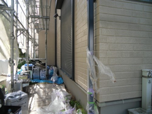 koushin_CIMG2664 | 外壁塗装は神奈川県横浜市の塗装職人 Construction area along the building's side with scaffolding, plastic sheeting, and scattered bags and tools.