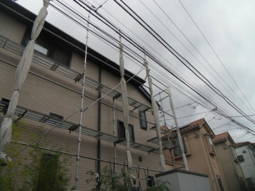 koushin_CIMG2667 | 外壁塗装は神奈川県横浜市の塗装職人 Construction scaffolding along the side of a beige house, with white wrap and overhead power lines.