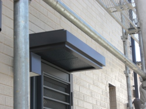 koushin_CIMG2674 | 外壁塗装は神奈川県横浜市の塗装職人 Metal overhang above a doorway on a beige brick wall with scaffolding nearby.
