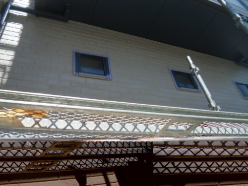 koushin_CIMG2684 | 外壁塗装は神奈川県横浜市の塗装職人 Underside view of a metal lattice railing and bridge above a beige brick wall with three small square windows.