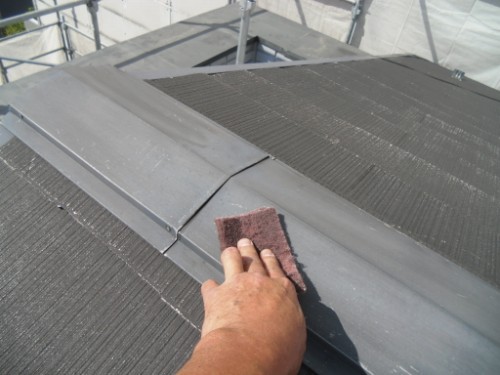koushin_CIMG2921-1 | 外壁塗装は神奈川県横浜市の塗装職人 Person's hand scrubs a seam on a dark metal roof with a brown cloth; scaffolding is visible in the background.