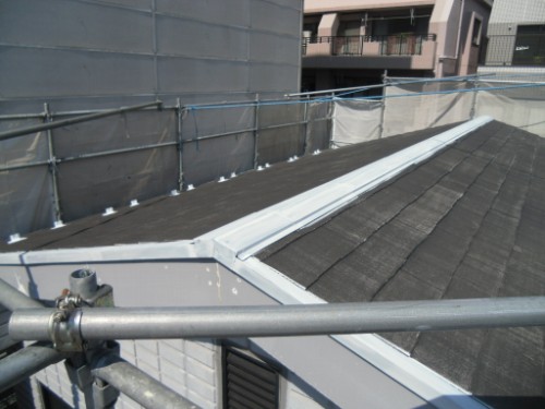 Rooftop under construction with metal scaffolding along the edge and gray shingles on the roof. White flashing lines the ridge.