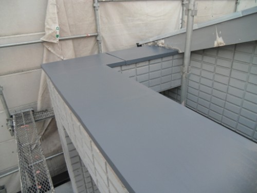 koushin_CIMG2934-1 | 外壁塗装は神奈川県横浜市の塗装職人 Grey metal flashing along the edge of a concrete block wall at a construction site, with scaffolding and tarps nearby.