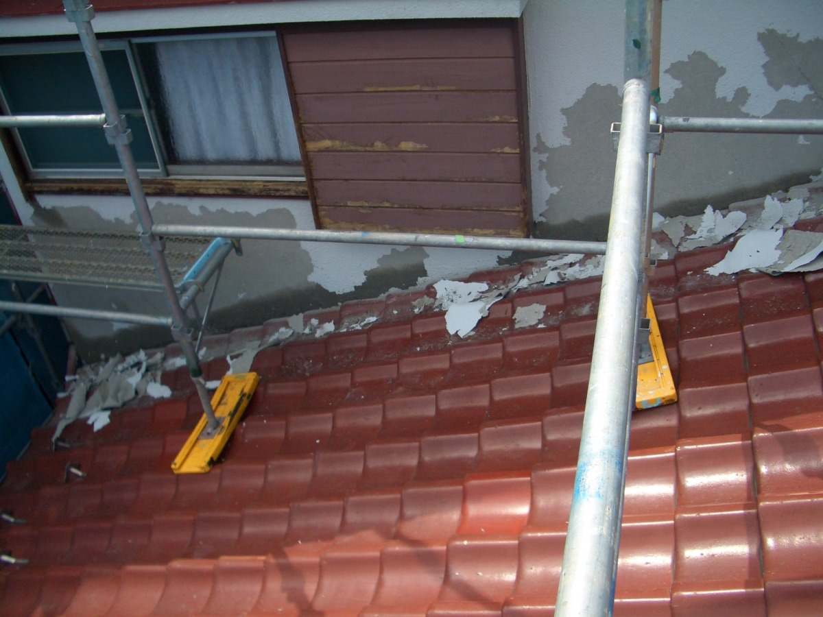 Metal scaffolding over a red tile roof; wall with peeling plaster beside a brown shuttered window.