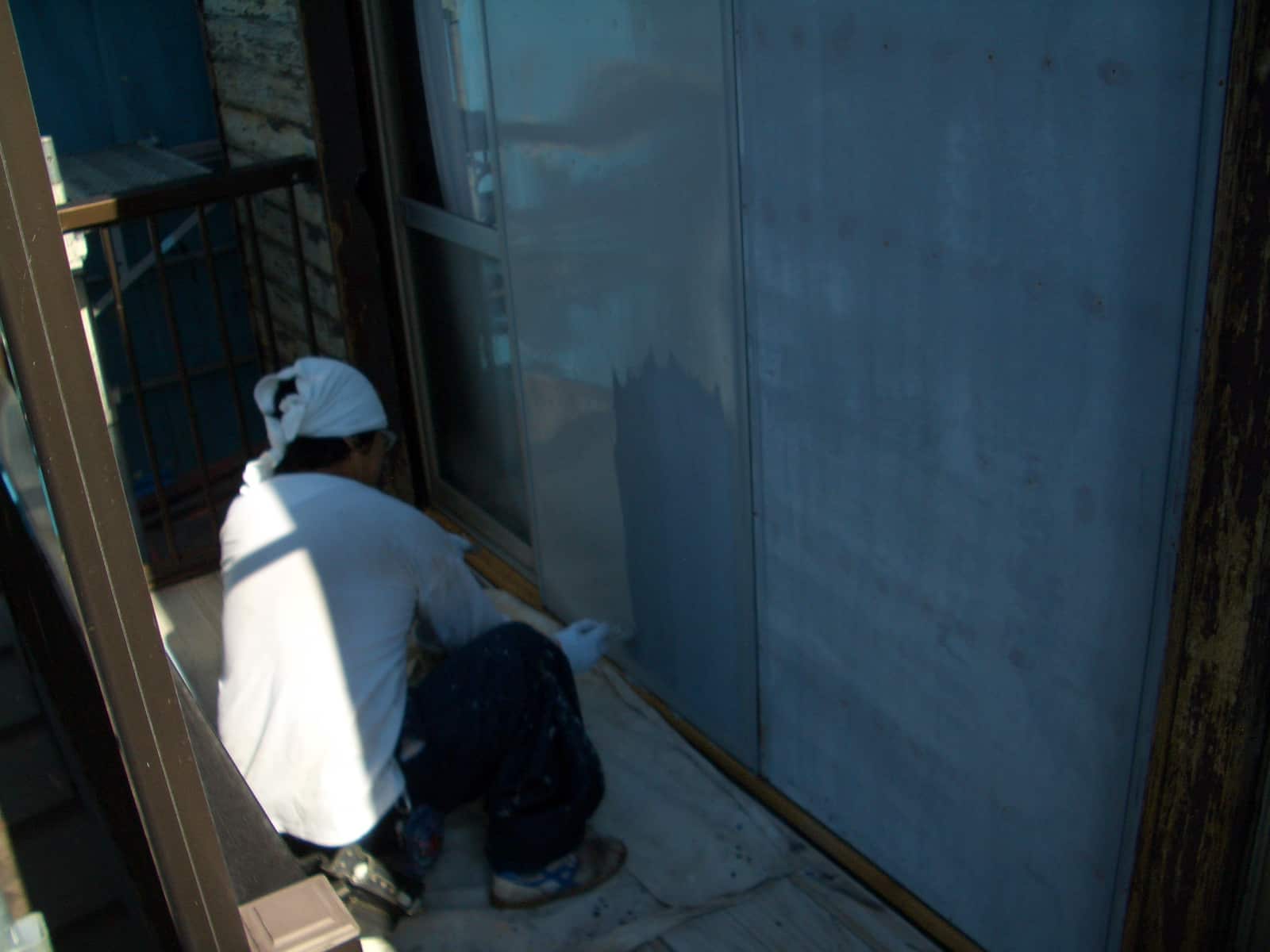 Construction worker crouches by a glass door frame, packing or smoothing material along the edge on a narrow balcony.