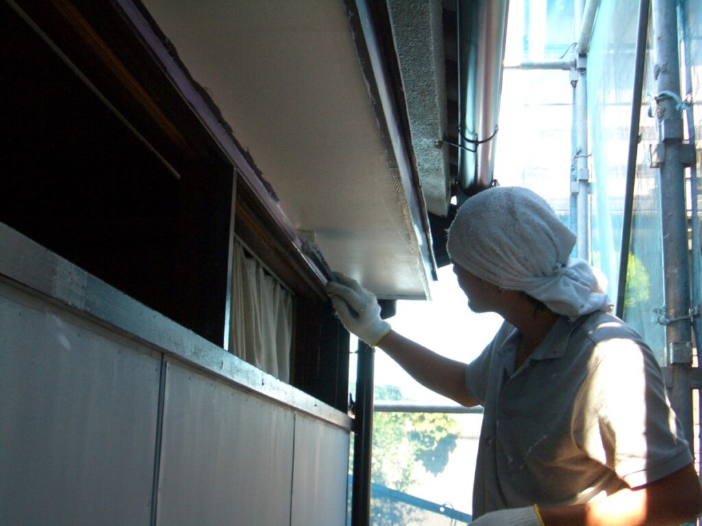Worker wearing a head wrap and gloves cleaning or inspecting the underside of a storefront awning from scaffolding outside, during daytime