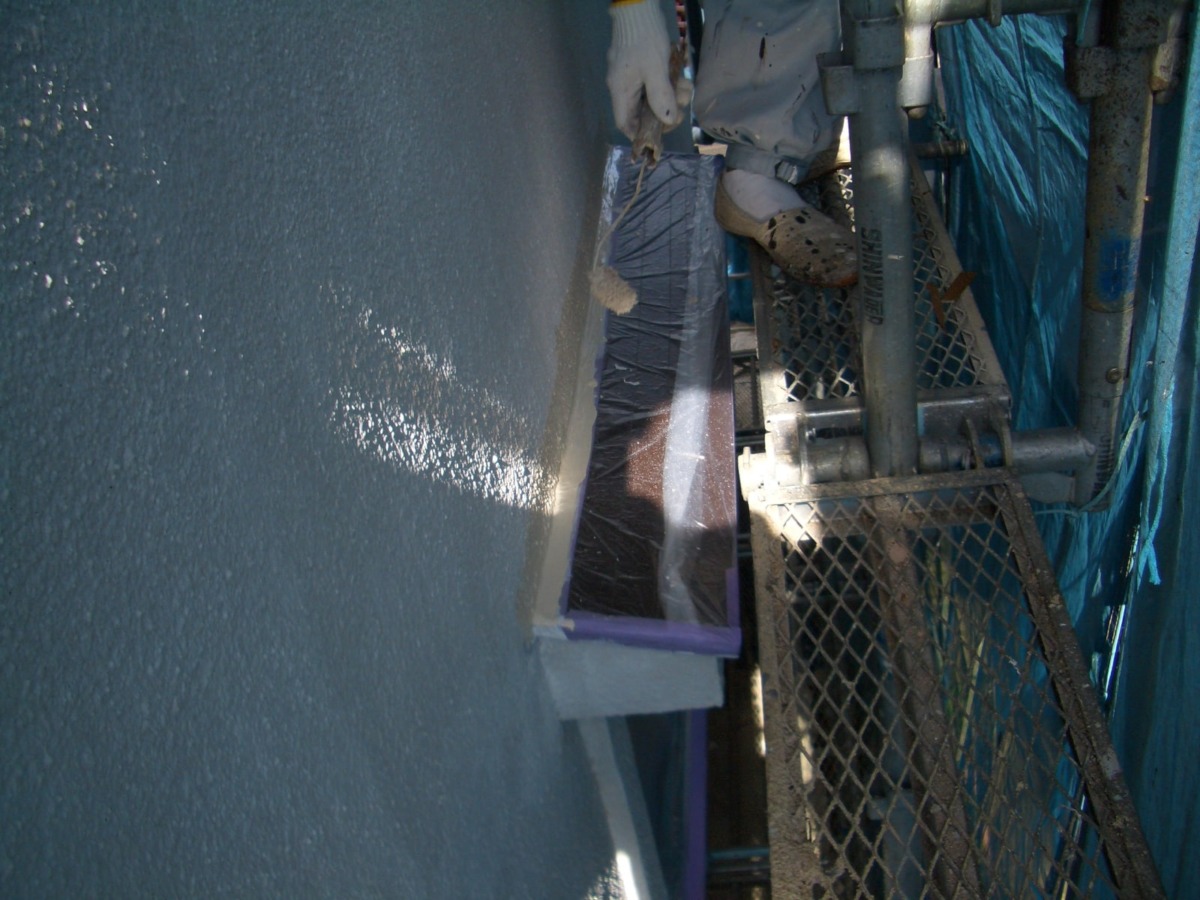 Worker wearing gloves paints an exterior blue wall from metal scaffolding.