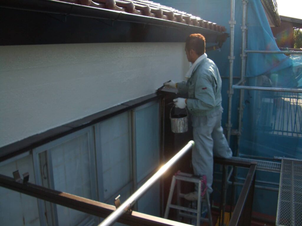 Worker in protective gear painting the exterior wall from scaffolding with a paint bucket and brush.