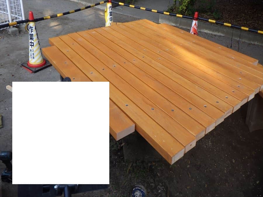 New wooden deck platform under construction, orange-brown planks bolted to a raised frame, with safety cones and caution tape around.