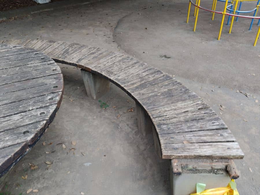 Curved, weathered wooden bench in a dusty playground with colorful metal bars in the background