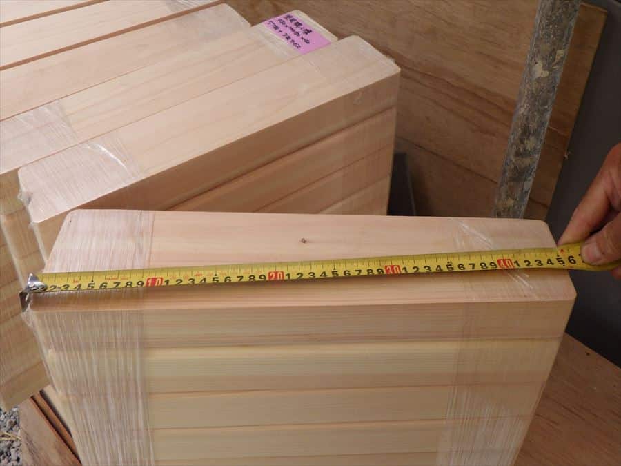 Measuring light wooden planks with a tape measure across their length in a lumber setting.