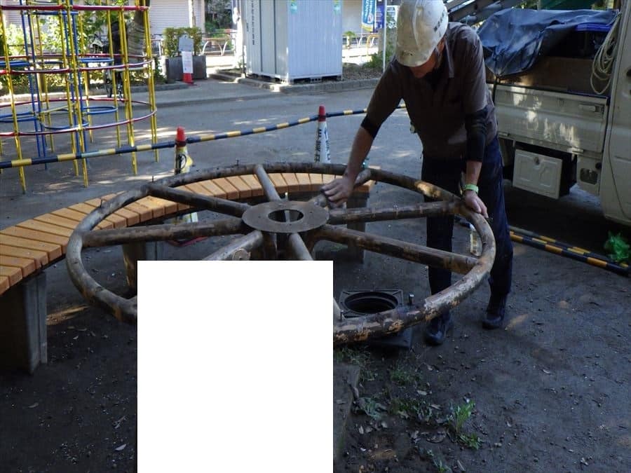 Construction worker wearing a helmet uses a large rusty circular valve wheel on an outdoor construction site
