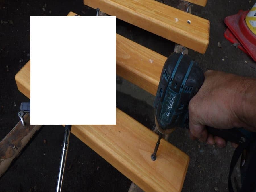 Person uses a cordless drill to drill into a wooden beam clamped to a workbench.